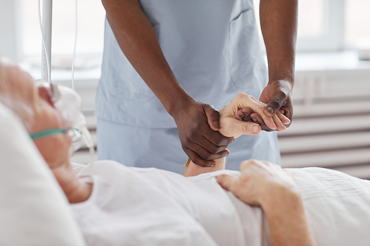 A hospice care nurse in a nursing home in Bossier City, LA holds a patient’s hand