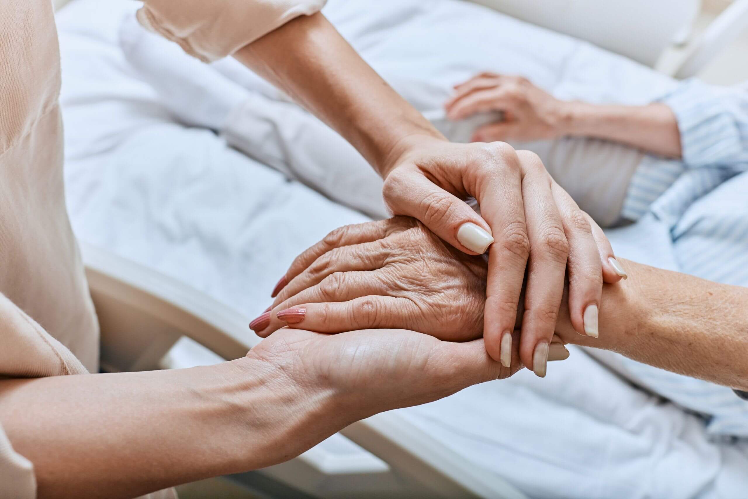 A woman offers empathetic palliative care, holding an elderly person's hand in a skilled nursing center in Bossier City