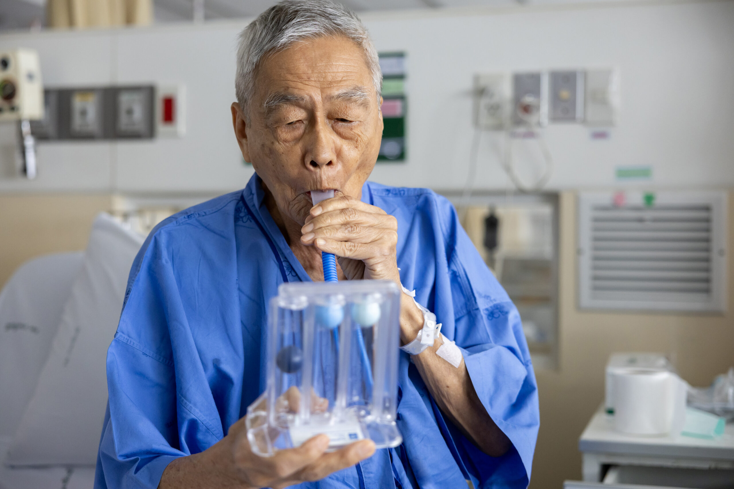 Senior asian man using incentive spirometer device for breathing exercise rehabilitation to recover from lung cancer after surgery due to heavy smoking in skilled nursing facility in Bossier City, LA